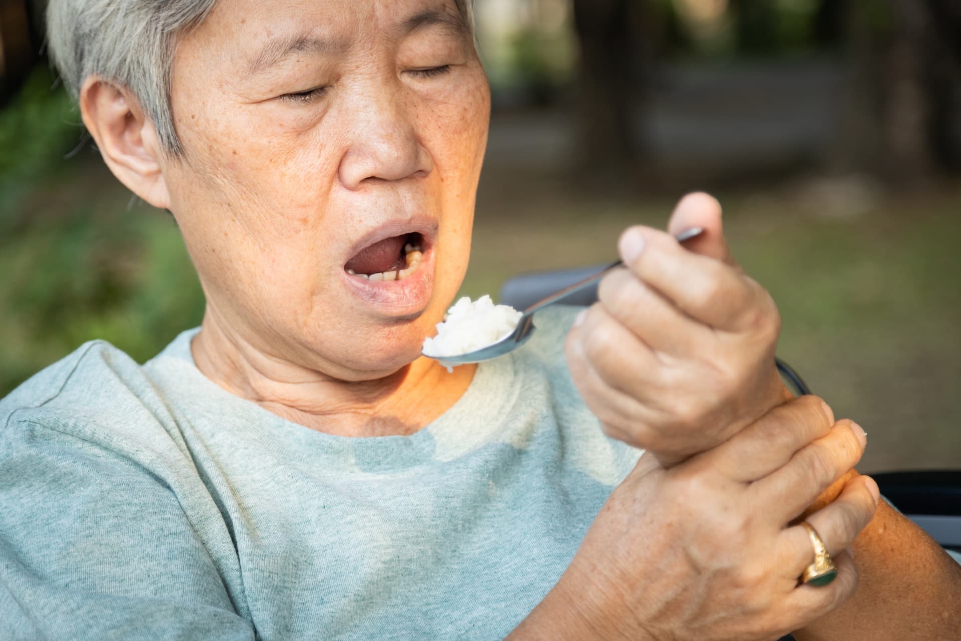 Asian senior woman holding spoon and hands tremor while eating